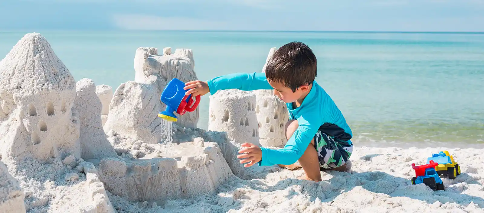 Boy building a sand castle while wearing a UPF sun protection shirt.